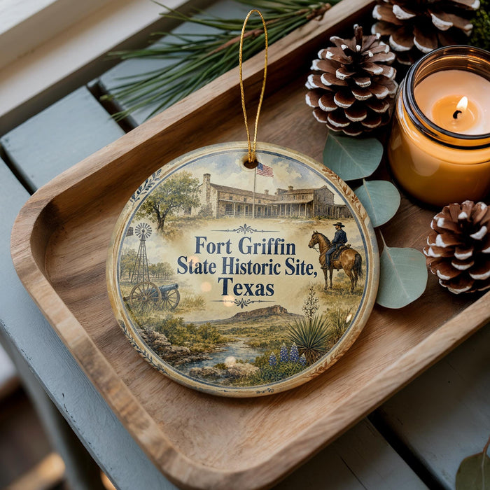 A decorative ornament with a picture of Fort Griffin, a historic site in Texas, sits on a wooden tray alongside pine cones and a lit candle.