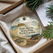 A round ornament with a picture of Fort Macon State Park, North Carolina, featuring a cannon and a turtle, is displayed in a box with pine branches.