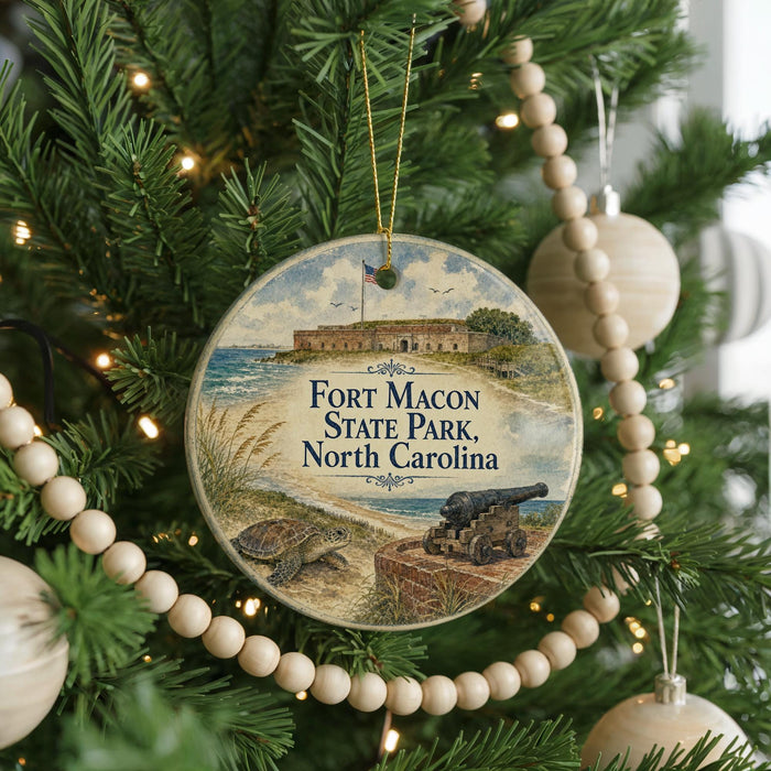 A round ornament hanging on a Christmas tree, featuring a picture of Fort Macon State Park in North Carolina.