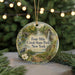 A round ornament with a scenic illustration of a park, featuring a waterfall, trees, and a bird, is displayed in front of a blurred background with Christmas lights.