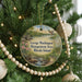 A round ornament hanging on a Christmas tree, featuring a scenic landscape with a lake, mountains, and a bird in flight.