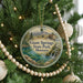 A round ornament on a Christmas tree, featuring a scenic image of the Grand Springs State Park in Montana.