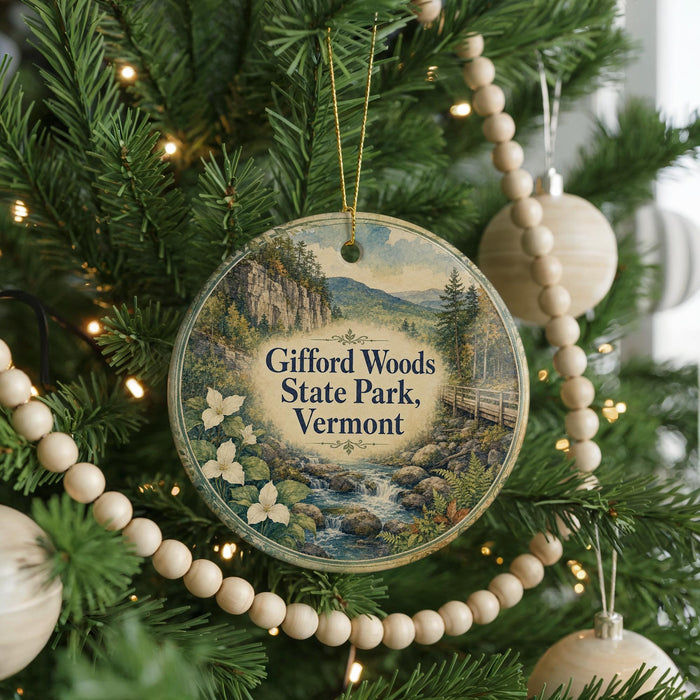 A round ornament hanging on a Christmas tree, featuring a scenic landscape with a river, mountains, and flowers.