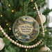 A round ornament hanging on a Christmas tree, featuring a scenic landscape with a river, mountains, and flowers.
