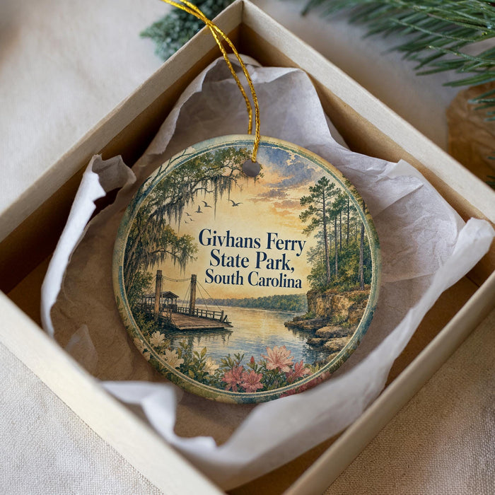 A decorative ornament in a box, featuring a scenic landscape with a river, trees, and a boat, along with the text "Givhan's Ferry State Park, South Carolina".