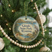 A round ornament hanging on a Christmas tree, featuring a scenic landscape with mountains, a lake, and a bird.