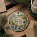 A round ornament with a scenic landscape of Glimmerglass State Park, New York, featuring a lake, a sailboat, and pine trees.