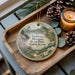 A wooden tray with a decorative ornament featuring a bird perched on a tree branch, surrounded by pine cones and a lit candle.
