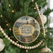 A round ornament hanging on a Christmas tree, featuring a scenic landscape with a dome-shaped building and a path leading to a body of water.