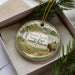 A decorative ornament in a box, featuring a scenic image of Good Earth State Park in South Dakota.