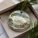 A decorative ornament in a box, featuring a landscape with a lake, mountains, and a bird in flight.