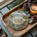 A decorative ornament with a scenic landscape of Goose Lake State Recreation Area Oregon, featuring a bird in flight and a cabin in the background. The ornament is placed on a wooden tray, with pine cones and a lit candle nearby.