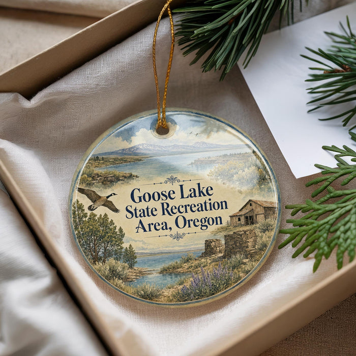 A decorative ornament with a landscape scene and a goose in flight, placed in a box with pine branches.