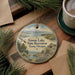 A decorative ornament with a scenic landscape featuring a lake, mountains, and a bird in flight, hanging on a wooden surface.