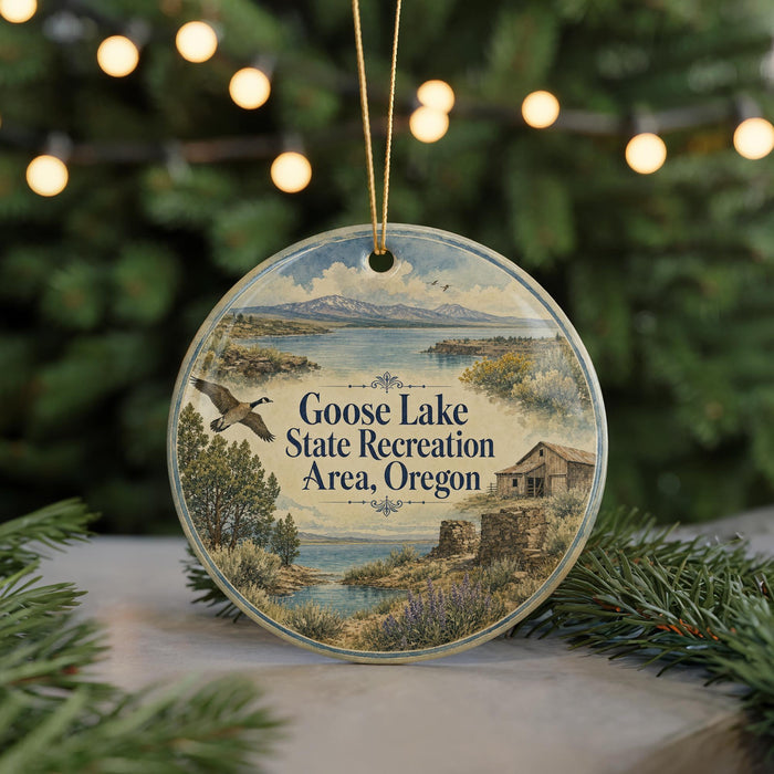 A circular ornament with a scenic landscape featuring a lake, mountains, and a bird in flight, hanging from a string.