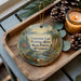 A wooden tray with a decorative ornament featuring a scenic image of the Poshtig River and Wisconsin, along with pine cones and a lit candle.