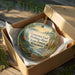 A wooden box containing a decorative ornament with a scenic landscape of a river, forest, and mountains.