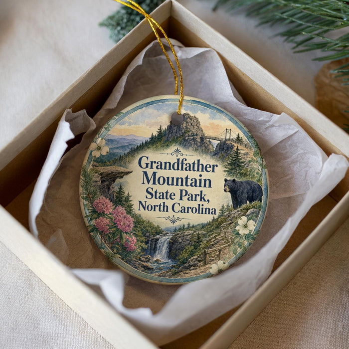 A decorative ornament in a box, featuring a scenic landscape with a waterfall, pine trees, and a bear.