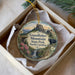 A decorative ornament in a box, featuring a scenic landscape with a waterfall, pine trees, and a bear.