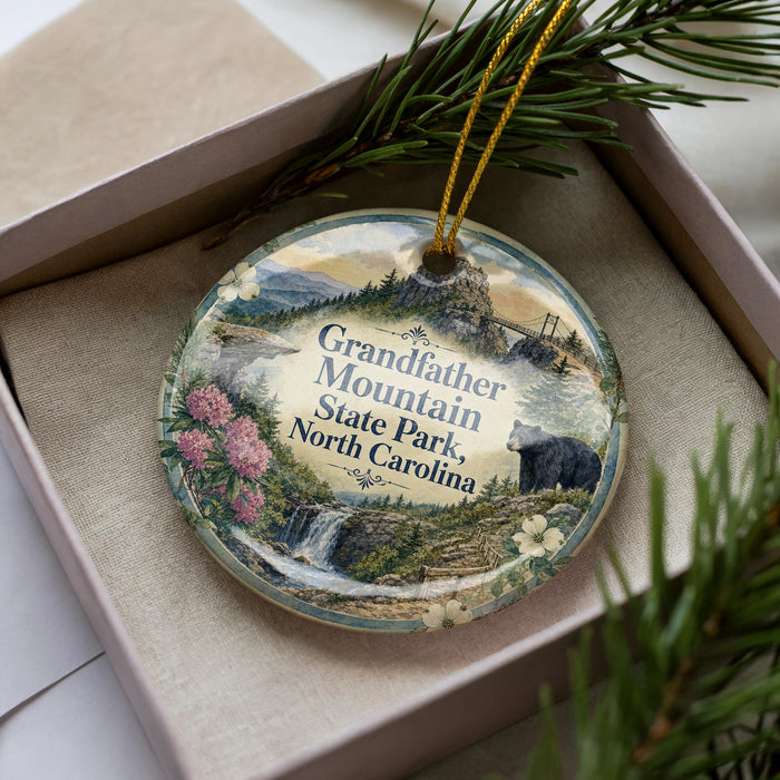 A decorative ornament in a box, featuring a scenic landscape with a bear, pine trees, and a waterfall.