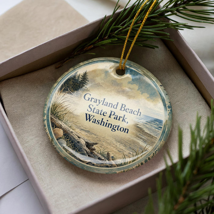 A circular ornament with a beach scene and text, placed in a box with pine branches.