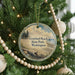A round ornament hanging on a Christmas tree, featuring a scenic image of a beach and a pine tree.