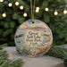 A round ornament with a scenic image of a lake and mountains, featuring a bird, is displayed in front of a blurred background with Christmas lights.