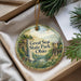 A decorative ornament with a scenic landscape of a waterfall and a building, surrounded by greenery, placed in a box with pine branches.