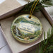 A decorative ornament with a scenic landscape of Greenfield State Park, New Hampshire, featuring a waterfall and a bridge.