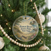 A round ornament hanging on a Christmas tree, featuring a scenic landscape with a lighthouse and a beach.