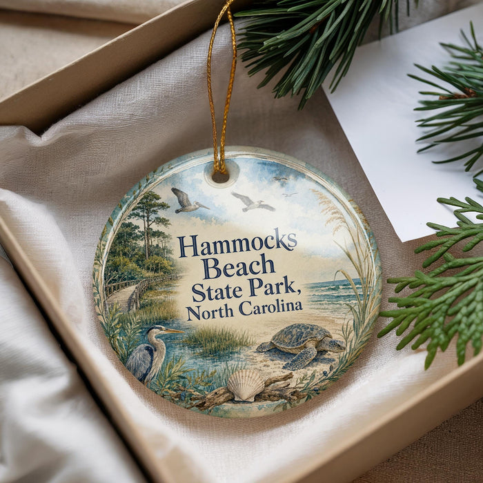 A decorative ornament with a beach scene and birds, placed in a box with pine branches.