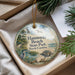 A decorative ornament with a beach scene and birds, placed in a box with pine branches.