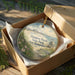 A decorative ornament in a box, featuring a beach scene with a lifeguard tower and a path leading to the beach.