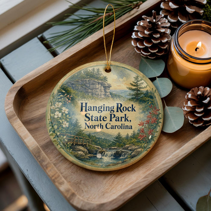 A wooden tray with a decorative ornament featuring a scenic landscape of hanging rock, pine trees, and a waterfall, accompanied by pine cones and a lit candle.
