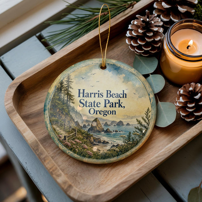 A decorative ornament featuring a scenic landscape of Harris Beach State Park, Oregon, with pine cones and a lit candle on a wooden tray.