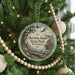 A round ornament hanging on a Christmas tree, featuring a scenic landscape with a lake and mountains.