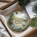 A decorative ornament with a scenic lake and park landscape, featuring a heron and a duck, is displayed in a box with pine branches.