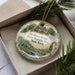 A decorative ornament in a box, featuring a historical scene with a building, a person, and a horse.