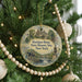 A round ornament hanging on a Christmas tree, featuring a painting of a historical building and a statue.