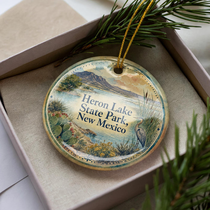 A decorative ornament in a box, featuring a scenic landscape with mountains, cacti, and a bird, along with the text "Heron Lake State Park, New Mexico".