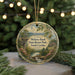 A round ornament with a scenic landscape featuring a waterfall, pine trees, and a cliff, hanging from a string.