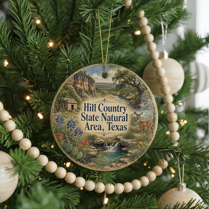 A round ornament hanging on a Christmas tree, featuring a scenic landscape with a river, mountains, and a deer.