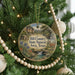 A round ornament hanging on a Christmas tree, featuring a scenic landscape with a river, mountains, and a deer.