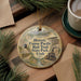 A decorative ornament featuring illustrations of a train, bridge, and natural scenery, with the text "Historic Union Pacific Rail Trail State Park, Utah" printed on it. The ornament is placed on a wooden surface, surrounded by pine branches and a cup of coffee.