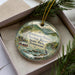 A decorative ornament with a scenic river and mountains in the background, featuring a boat and people enjoying the river.