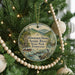 A round ornament hanging on a Christmas tree, featuring a scenic river and mountains in the background.