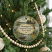 A round ornament hanging on a Christmas tree, featuring a scenic landscape with a lake, trees, and wildlife.
