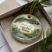 A decorative ornament in a box, featuring a scenic landscape with a lake, trees, and wildlife.