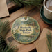 A decorative ornament with a scenic image of a park, featuring a bird, a cabin, and a lake, hangs on a wooden surface.