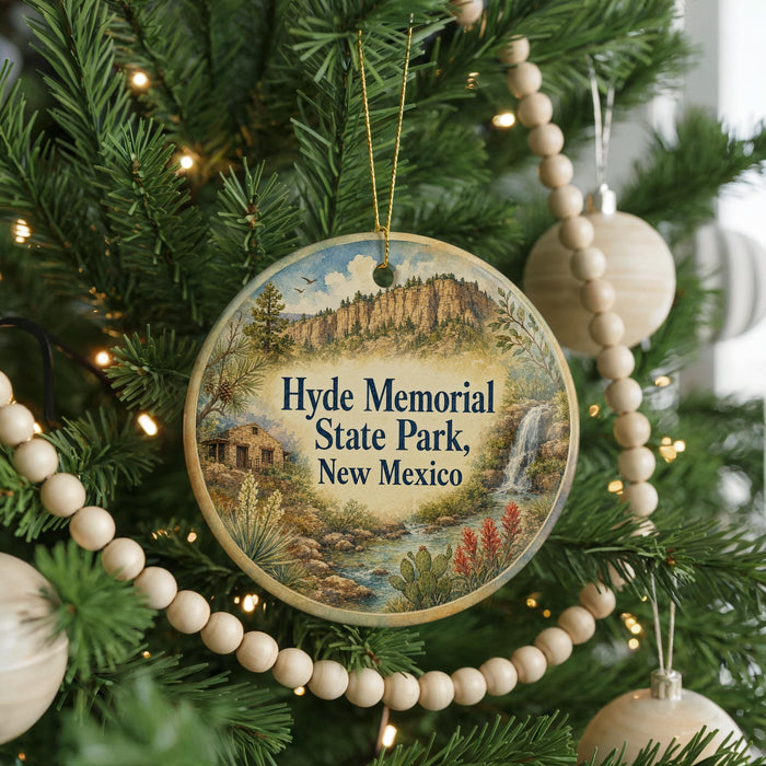 A round ornament hanging on a Christmas tree, featuring a scenic landscape with a waterfall and mountains.